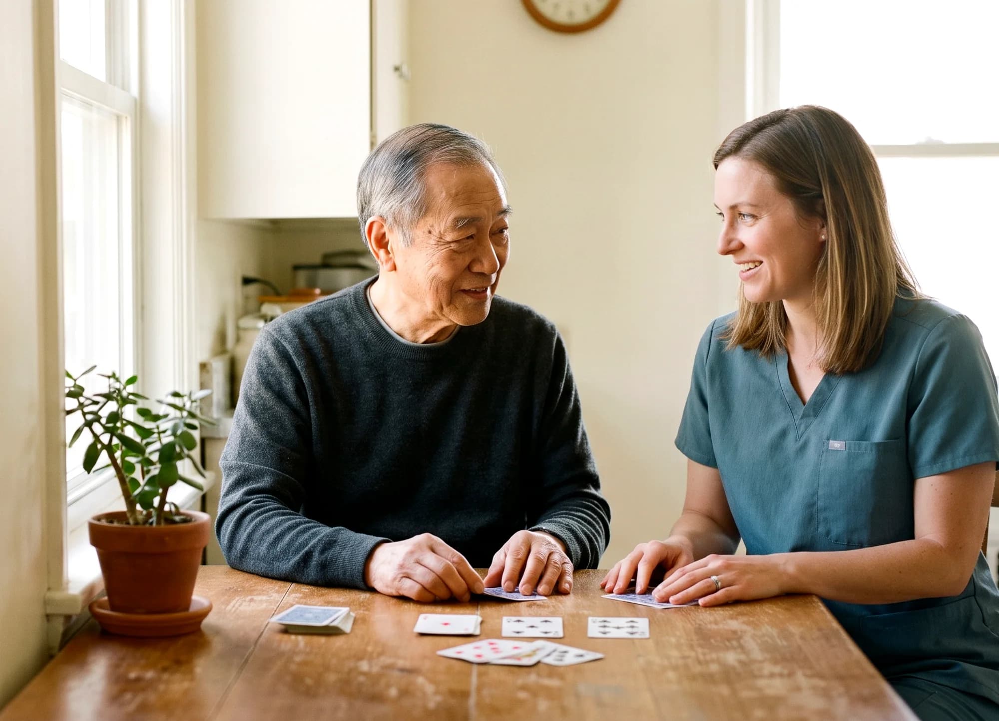 A caregiver playing cards at the kitchen table with an older man